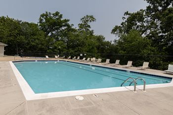 A large outdoor swimming pool surrounded by trees and lounge chairs.